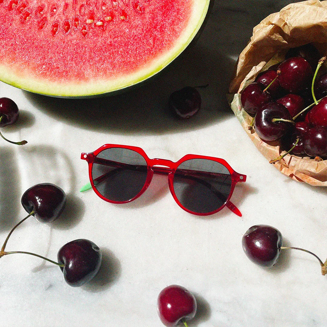 Photograph of a frame surrounded by a basket of cherries, scattered cherries, and a watermelon.
