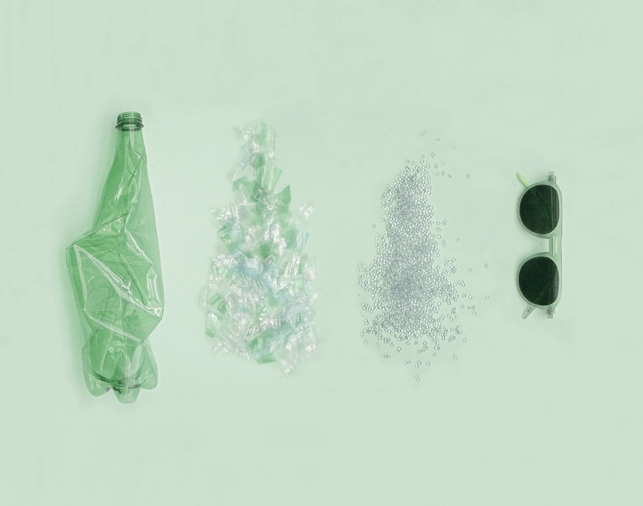 Photograph of an INFINITY frame depicting the plastic transformation process used in its manufacturing. From left to right, there is a green transparent plastic bottle, plastic bottle scraps, plastic granules, and the INFINITY frame.