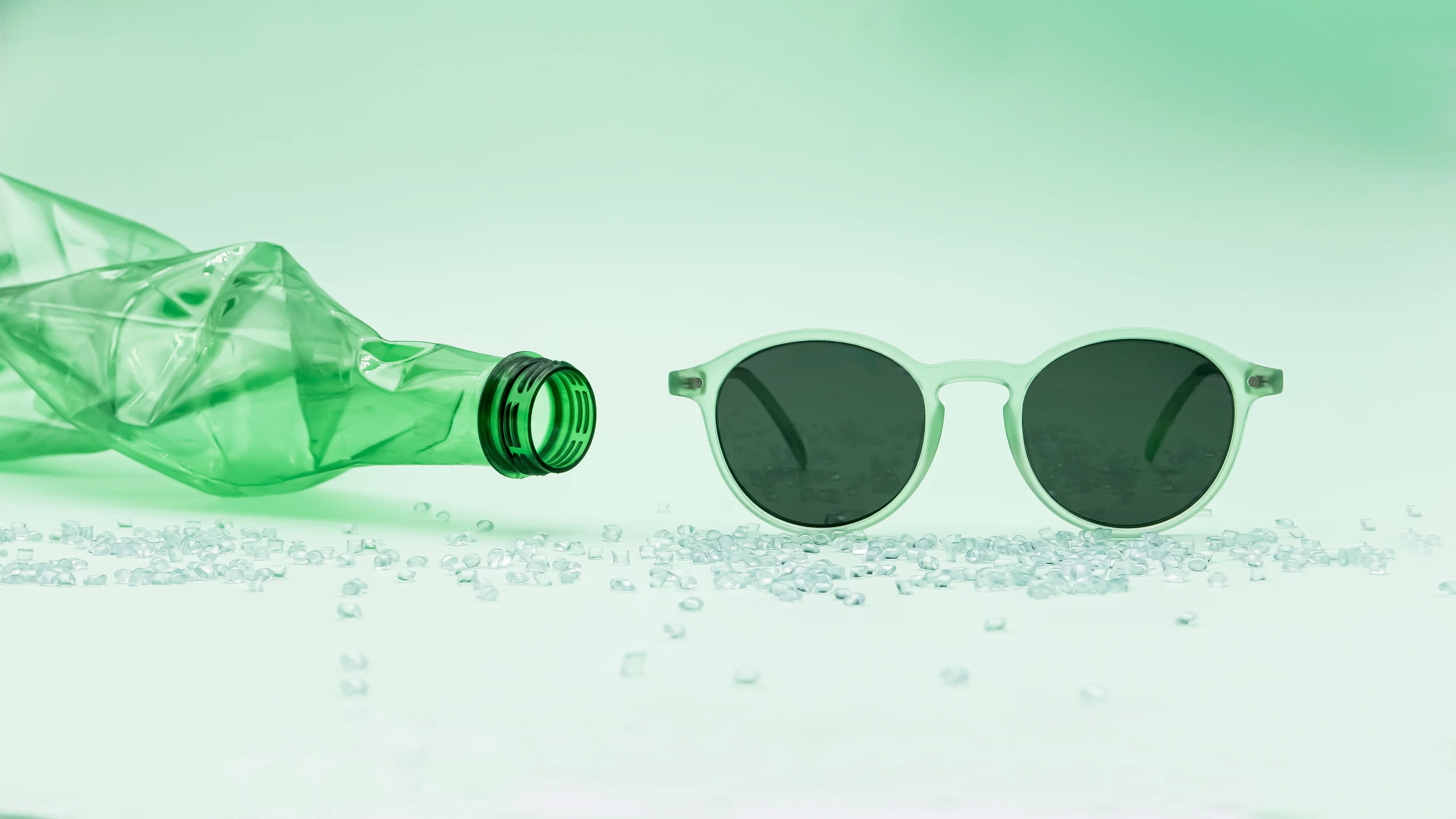 Photographie de la monture Melati couleur Pistache à côté d'une bouteille en plastique transparente verte et de granules de plastique verts. Les granules et la bouteille sont recyclés et utilisés pour créer la monture présente dans la photographie.